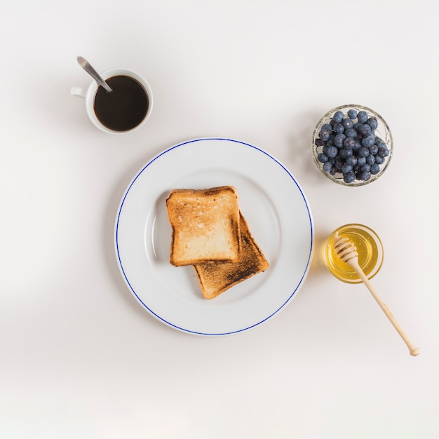 Tea cup; toast breads; honey and blueberries bowl on white backdrop