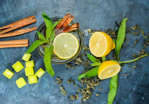 Tea in a cup with lemon, mint, cinnamon sticks, sugar cubes top view on a blue surface