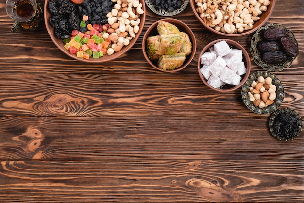 Tea; dried mixed fruits; nuts; lukum and baklava on earthen and metallic bowl on wooden desk