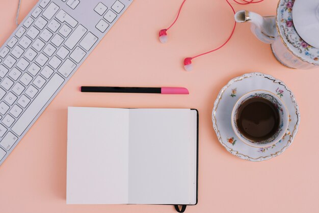 Tea and earphones near notebook and keyboard