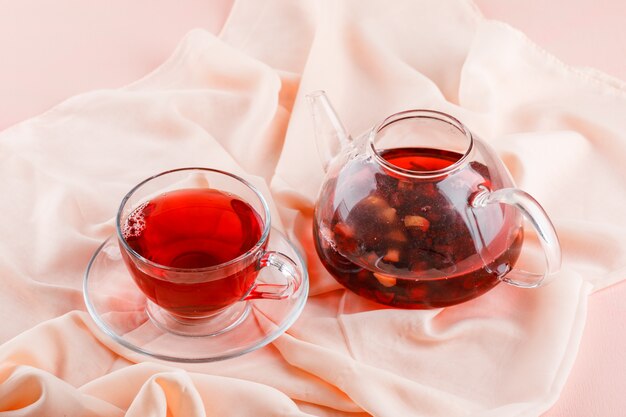 Tea in glass mug and teapot on pink and textile high.