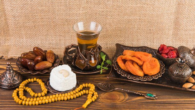 Tea glass with dried fruits and beads on wooden table