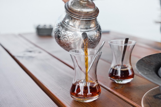 Чай наливают в стакан из традиционного турецкого чайника с селективным фокусом, пар поднимается от горячего напитка Завтрак в кафе, путешествие и время отдыха