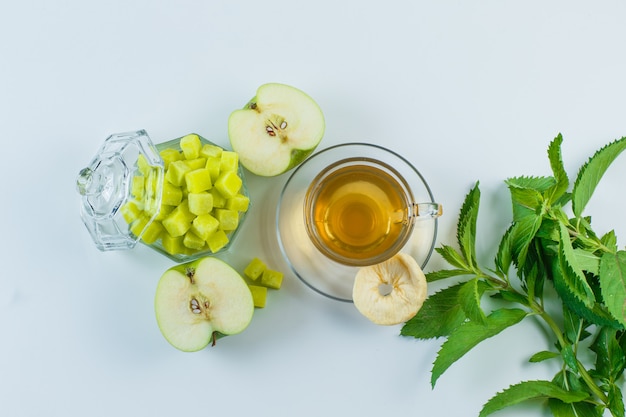 Tea in a mug with apple, dried fruit, sugar cubes, herbs flat lay on a white background