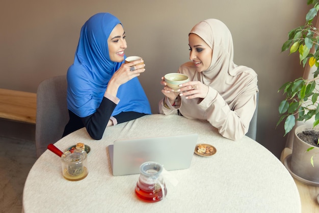 차 붓기. 카페나 레스토랑, 친구 또는 비즈니스 회의에서 만나는 아름다운 아랍 여성. 함께 시간을 보내고, 이야기하고, 웃고. 이슬람 라이프 스타일. 메이크업으로 세련되고 행복한 모델.