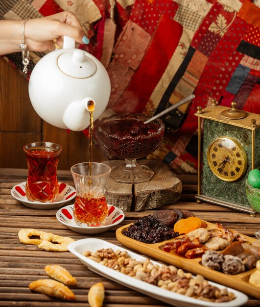 Tea set for 2 pax with dry fruits and sweets, white kettle, wooden table