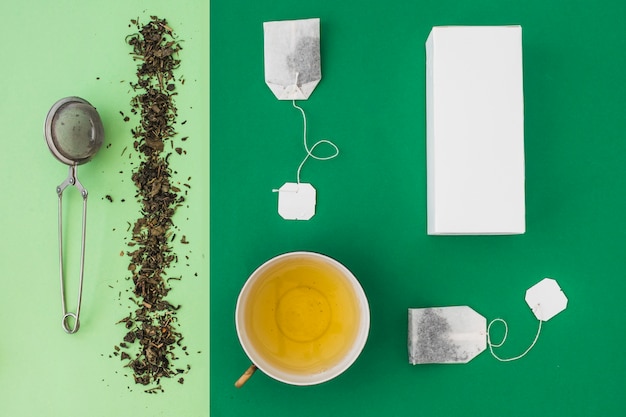 Setaccio del tè, bustina di tè e scatole bianche su fondo verde