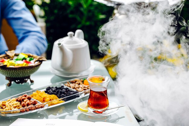 Tea table sweets nuts white kettle and steam.