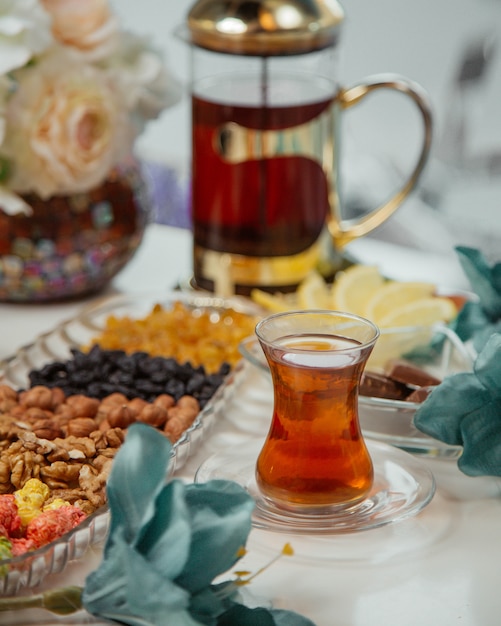 Чайный столик с конфетами и орехами и стакан чая.