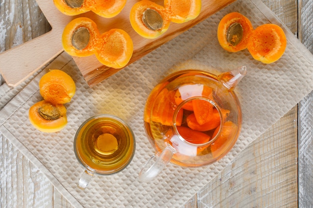 Tea in teapot and mug with apricots, cutting board top view on wooden and kitchen towel