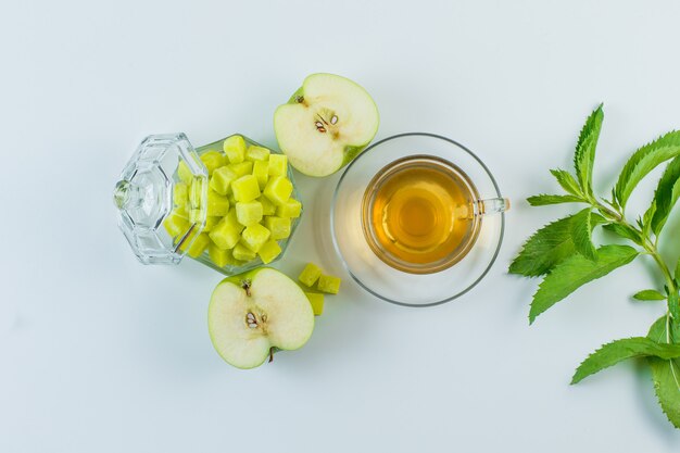 Tea with apple, sugar cubes, herbs in a mug on white background, flat lay.