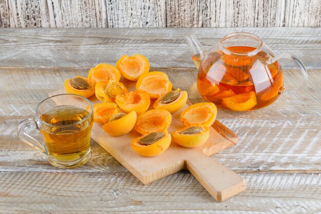 Tea with apricots in teapot and mug on wooden and cutting board, top view.