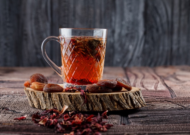 Tea with dried fruits and flowers, lemon, wood in a cup on stone tile and wooden surface