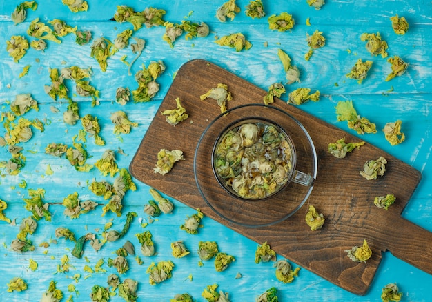 Tea with dried herbs in a glass mug on blue and cutting board, top view.