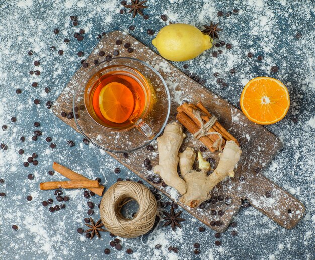 Free photo tea with flour, choco chips, thread, spices, orange, lemon in a mug on concrete and cutting board, top view.