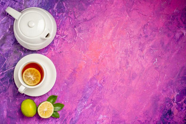 tea with lemon a cup of tea with lemon next to the teapot and limes on the left side of the pink-purple table