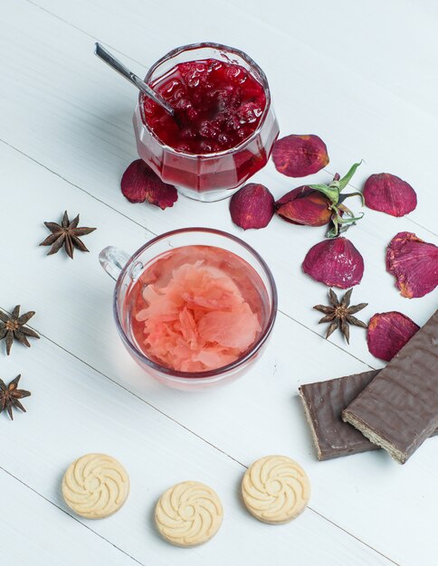 Tea with rose petals, jam, spice, cookies in a cup on wooden table, flat lay.