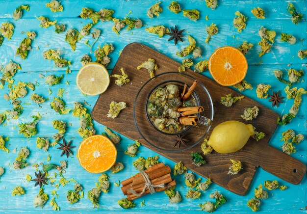 Tea with spices, orange, lemon, dried herbs in a mug on blue and cutting board, top view.