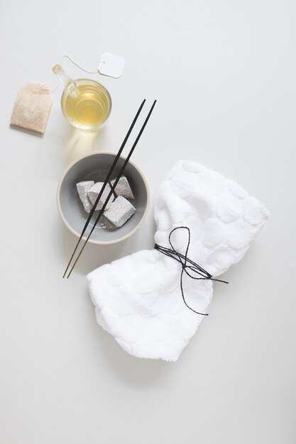 Чайный пакетик; масло; пемза; ароматическая палочка и перевязанная салфетка на белой поверхности