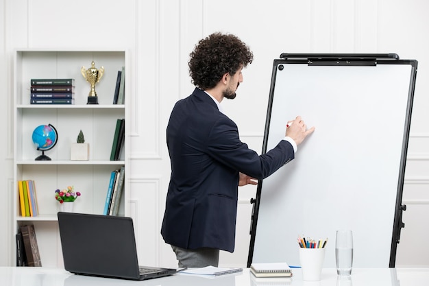 Free photo teacher brunette instructor with computer in suit and whiteboard in classroom drawing on board