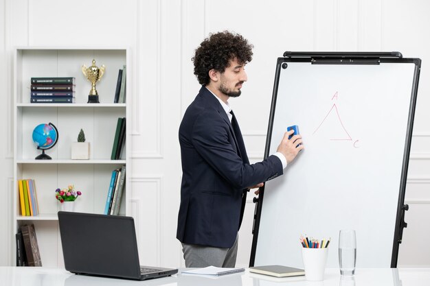 Teacher brunette instructor with computer in suit and whiteboard in classroom erasing board