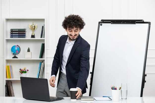 Teacher brunette instructor with computer in suit and whiteboard in classroom reaching cup