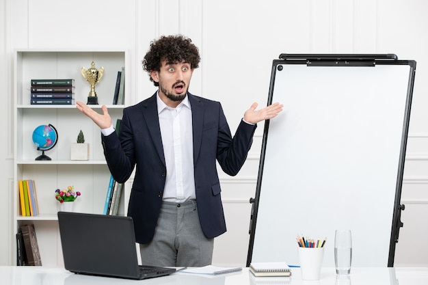 Teacher brunette instructor with computer in suit and whiteboard in classroom shocked waving hands