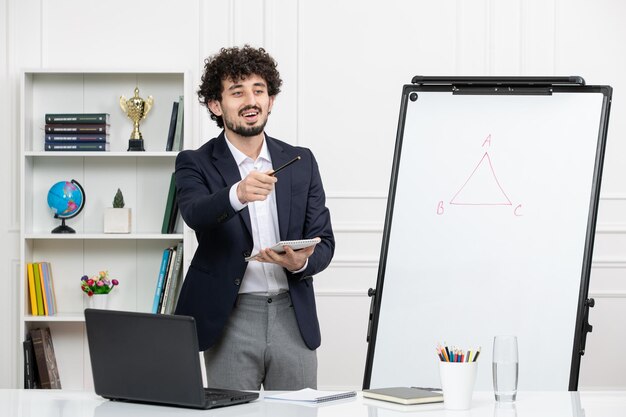 Teacher brunette instructor with computer in suit and whiteboard in classroom talking to student