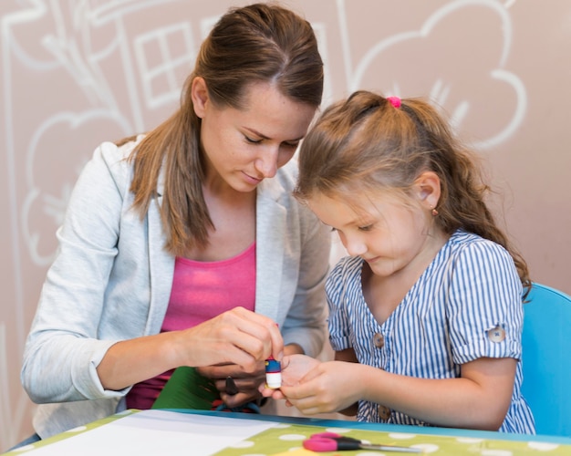 Teacher and girl gluing paper together