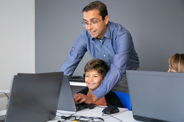 Free photo teacher in glasses explaining lesson to boy and standing behind him