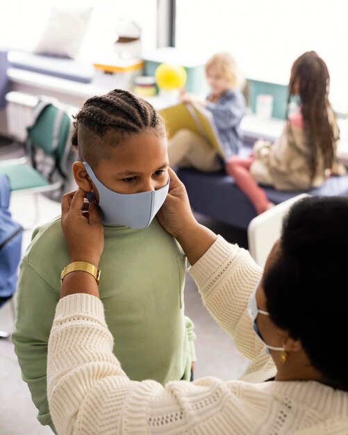 生徒が医療用マスクを着用するのを手伝う教師