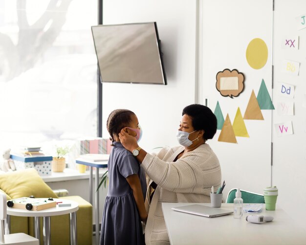 Teacher helping a student to put a medical mask on