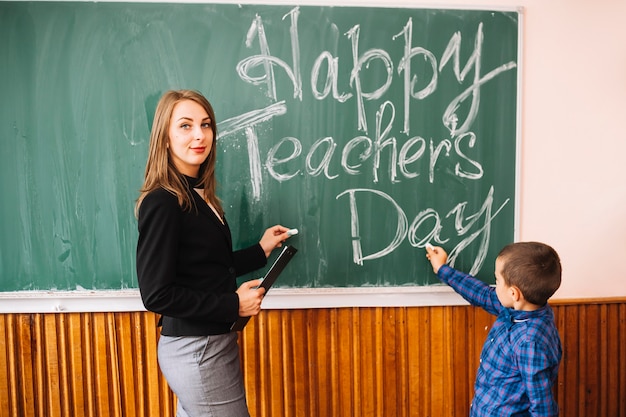 Teacher looking at camera with pupil at blackboard