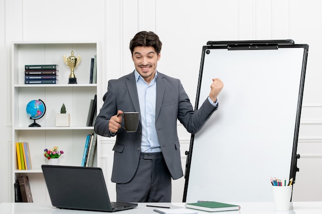 Teacher smart instructor in grey suit in classroom with computer and whiteboard excited