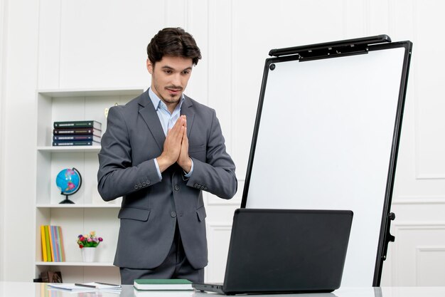 Teacher smart instructor in grey suit in classroom with computer whiteboard putting hands together