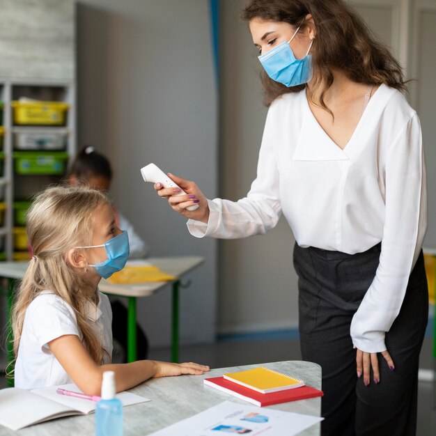 Teacher taking the temperature of a little girl