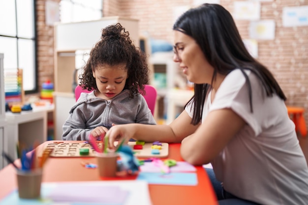 Free photo teacher and toddler playing with maths puzzle game sitting on table at kindergarten