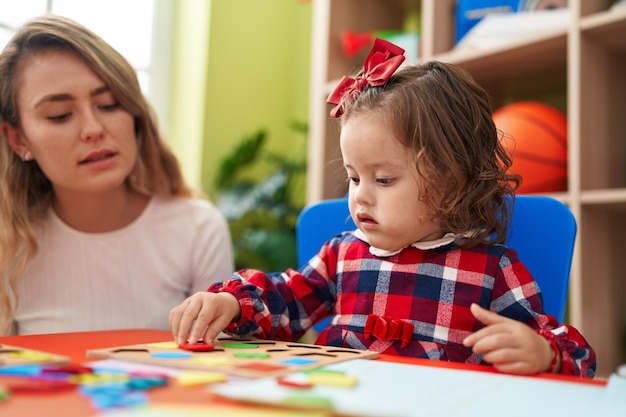 Teacher and toddler playing with maths puzzle game sitting on table at kindergarten