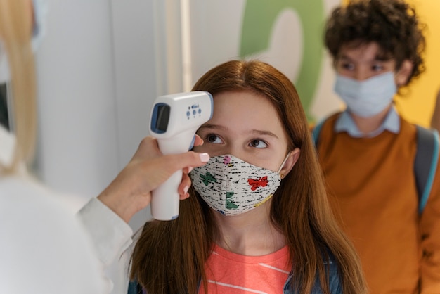 Insegnante con mascherina medica che controlla la temperatura dei bambini a scuola Foto Gratuite