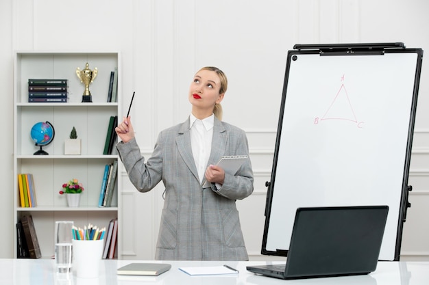 Foto gratuita insegnante giovane istruttore carino in tuta in classe con laptop e lavagna alzando lo sguardo