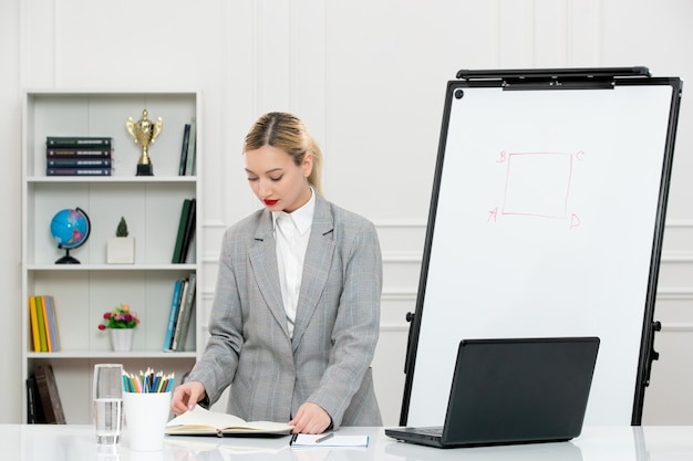 Free photo teacher young cute instructor in suit in classrom with laptop and whiteboard reading notes