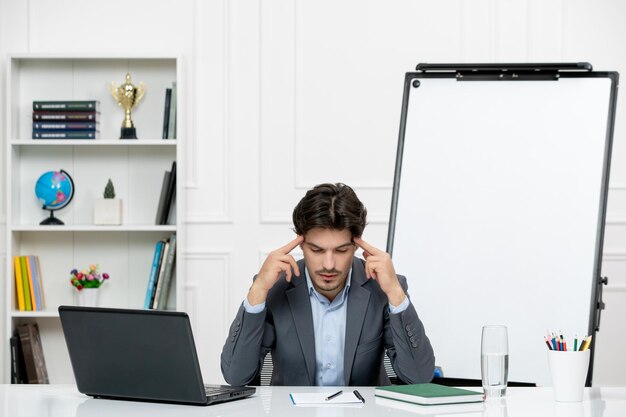 Teacher young instructor in office suit in the class with computer and whiteboard concentrated