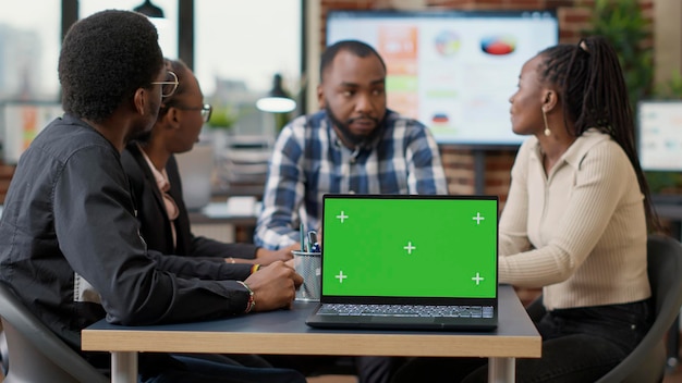 녹색 화면이 있는 노트북을 가지고 재정 전략을 하고 있는 아프리카계 미국인 팀. 격리된 복사 공간과 빈 모형 배경이 있는 크로마 키 템플릿을 사용하는 동료. 삼각대 샷.