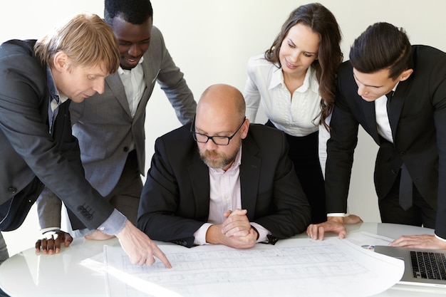 Team of architects studying blueprints during meeting while working on new engineering project.