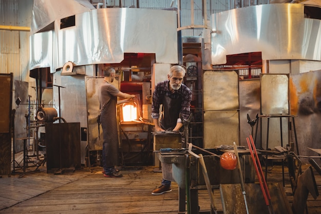 Team of glassblowers shaping a glass on the blowpipe