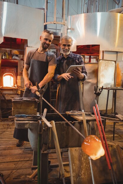 Team of glassblowers using digital while working over a molten glass