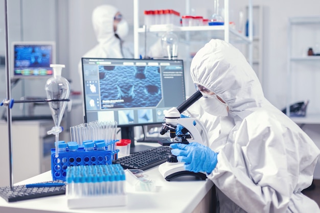 現代の実験室でコロナウイルス分析を行う医療用個人用ppeスーツのチーム。生化学実験室でのcovid-19チェックサンプルによる世界的大流行中の化学者研究者