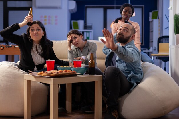 Команда многоэтнических друзей проигрывает телевизионную игру на консоли после работы в офисе