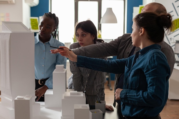 Free photo team of professional architects brainstorming ideeas pointing at real estate construction model in architectural office. mixed group of engineers working on residential project at desk.