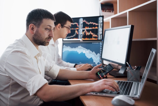 Team of stockbrokers are having a conversation in a dark office with display screens. Analyzing data, graphs and reports for investment purposes. Creative teamwork traders